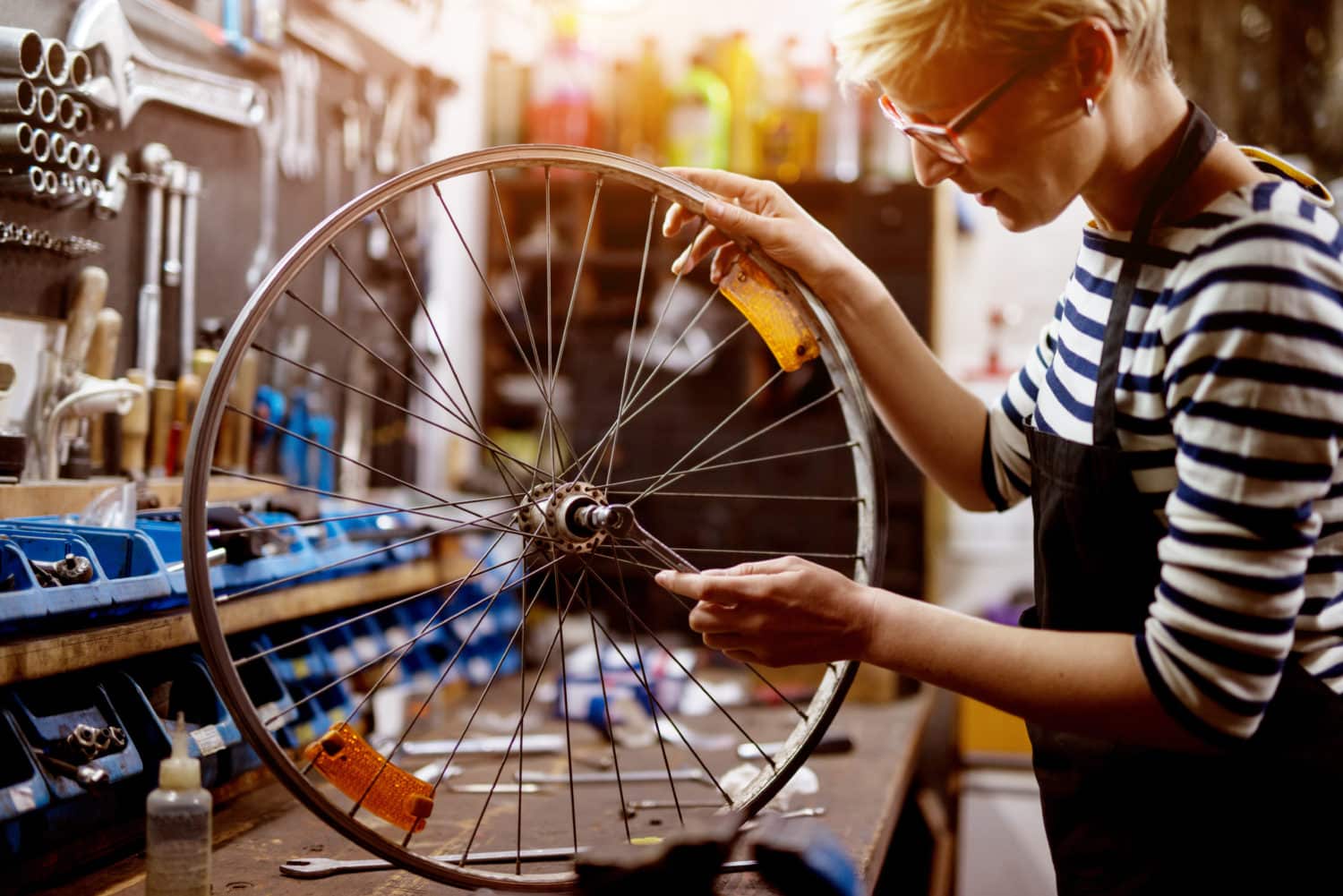 Beautiful focused woman checking bicycle tire with a wrench in the sunny garage.